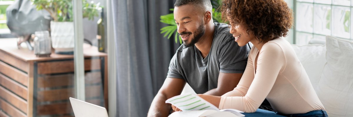 A couple sit in their living room and pay their credit card balances online.