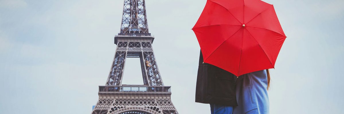 Couple standing behind red umbrella looking out at Eiffel Tower.