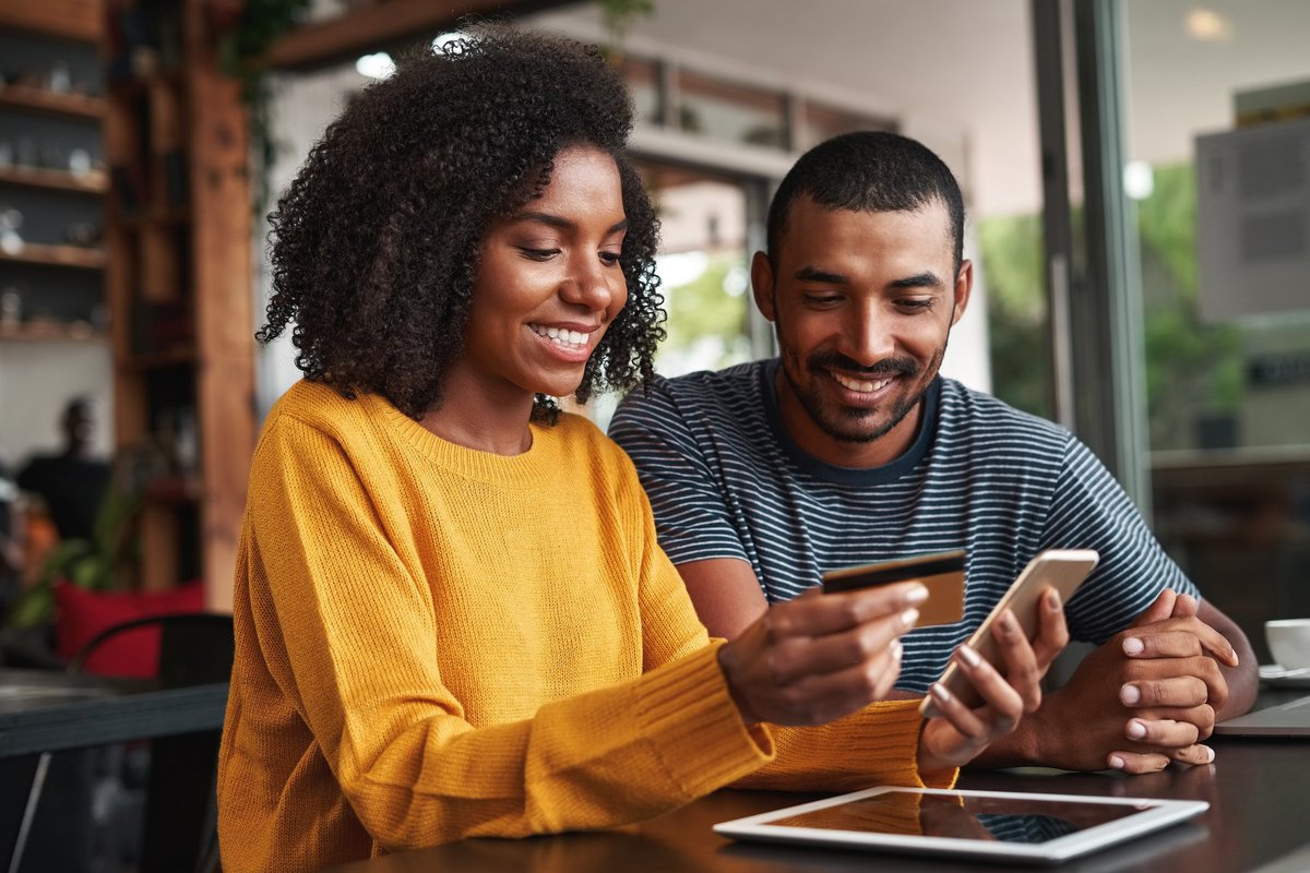 A smiling couple using a credit card for an online purchase.