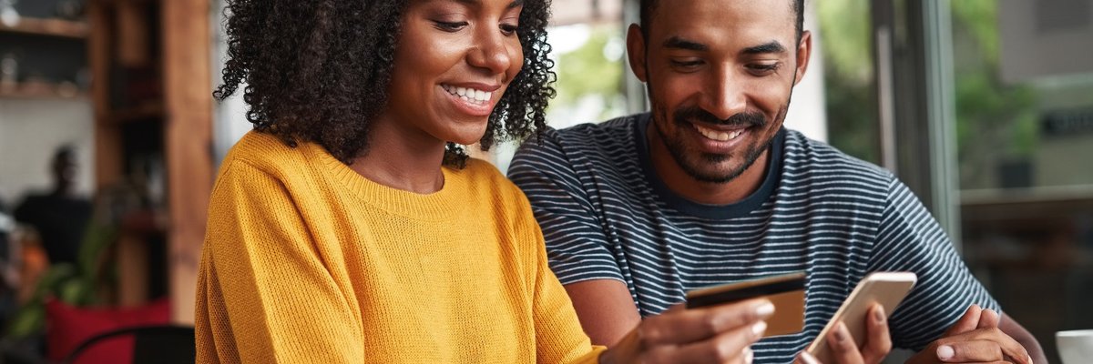 A smiling couple using a credit card for an online purchase.