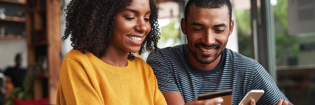 A smiling couple using a credit card for an online purchase.