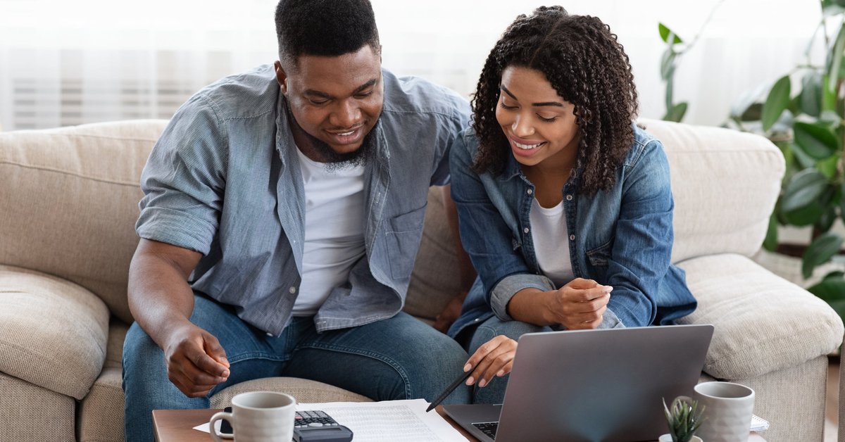 Couple using laptop and calculator together smiling.