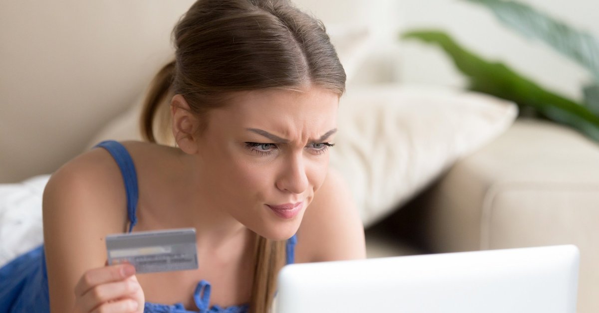 A woman looking confused at her computer while holding a credit card.