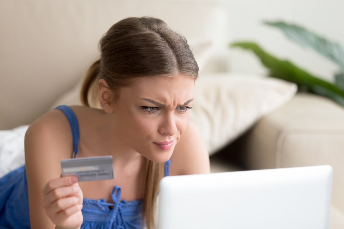 A woman looking confused at her computer while holding a credit card.