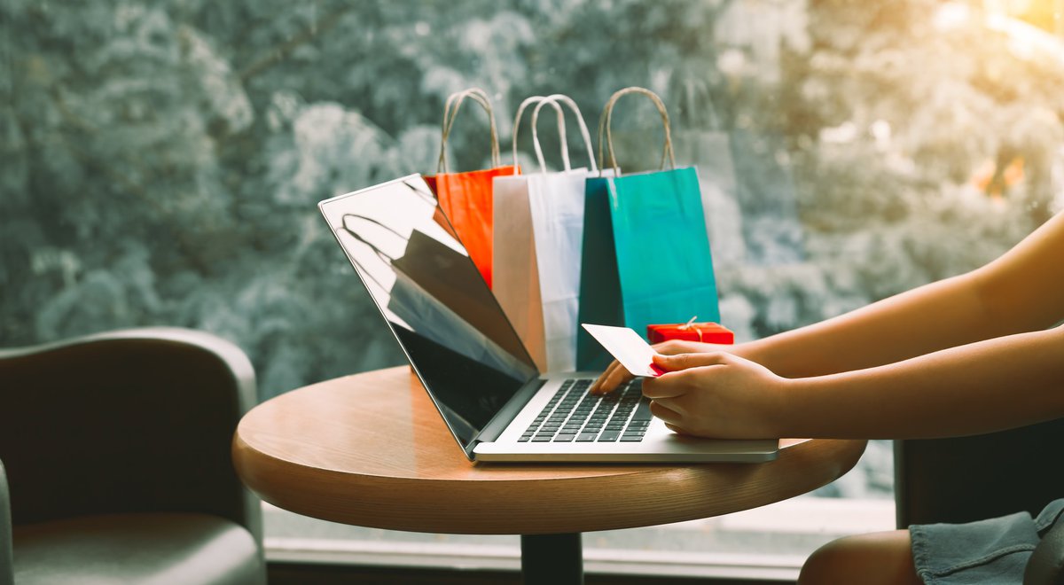 Someone using a credit card to shop on their laptop next to shopping bags on the table.