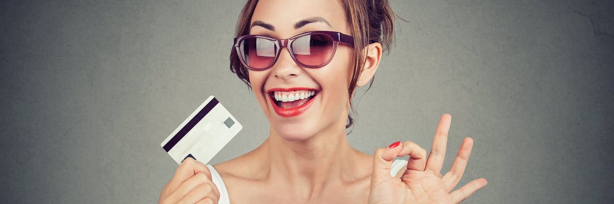 young woman in sunglasses holding a credit card and grinning