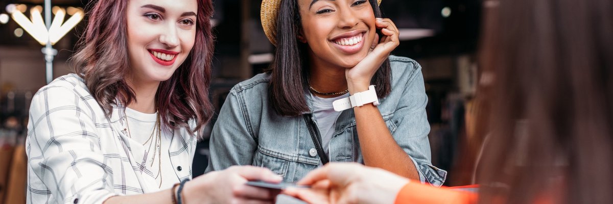 Two young women interact with cashier as one hands over a credit card.