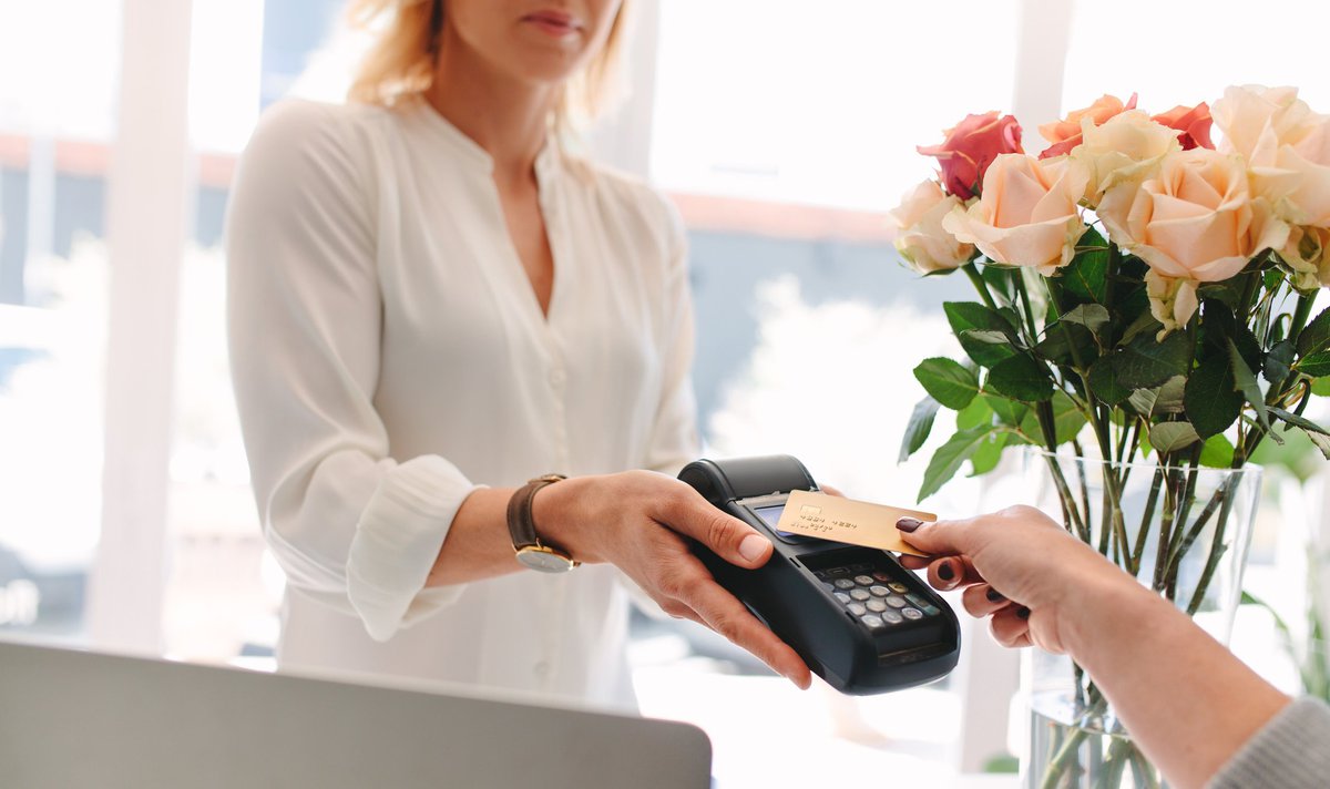Someone paying on a credit card reader with flowers in the background.