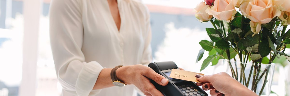 Someone paying on a credit card reader with flowers in the background.