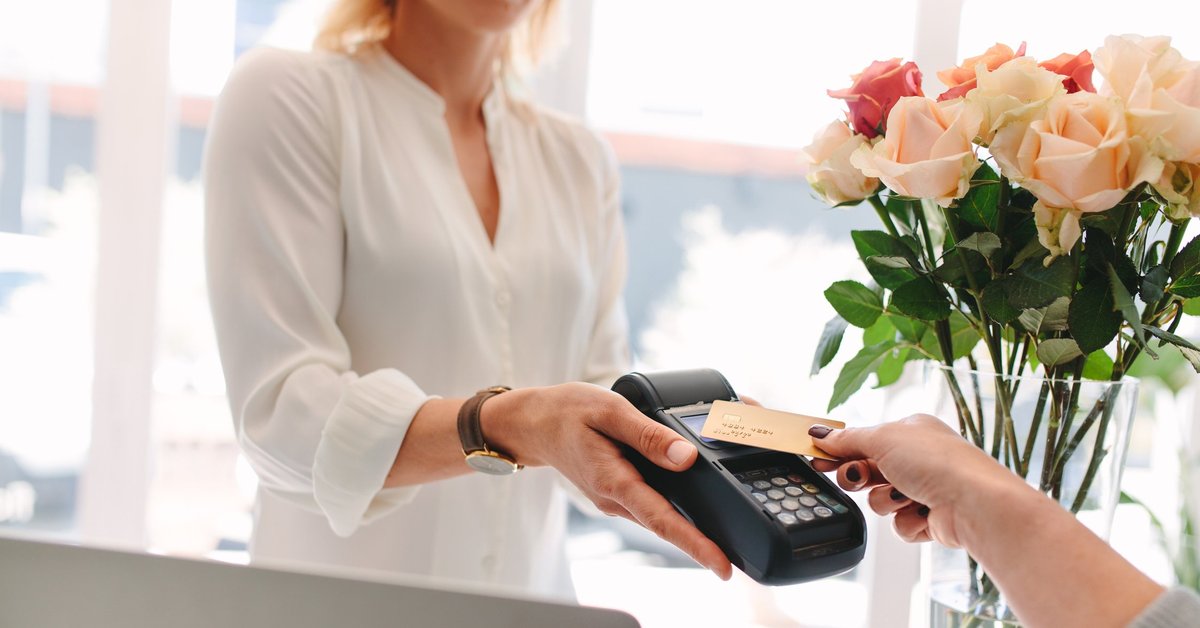 Someone paying on a credit card reader with flowers in the background.