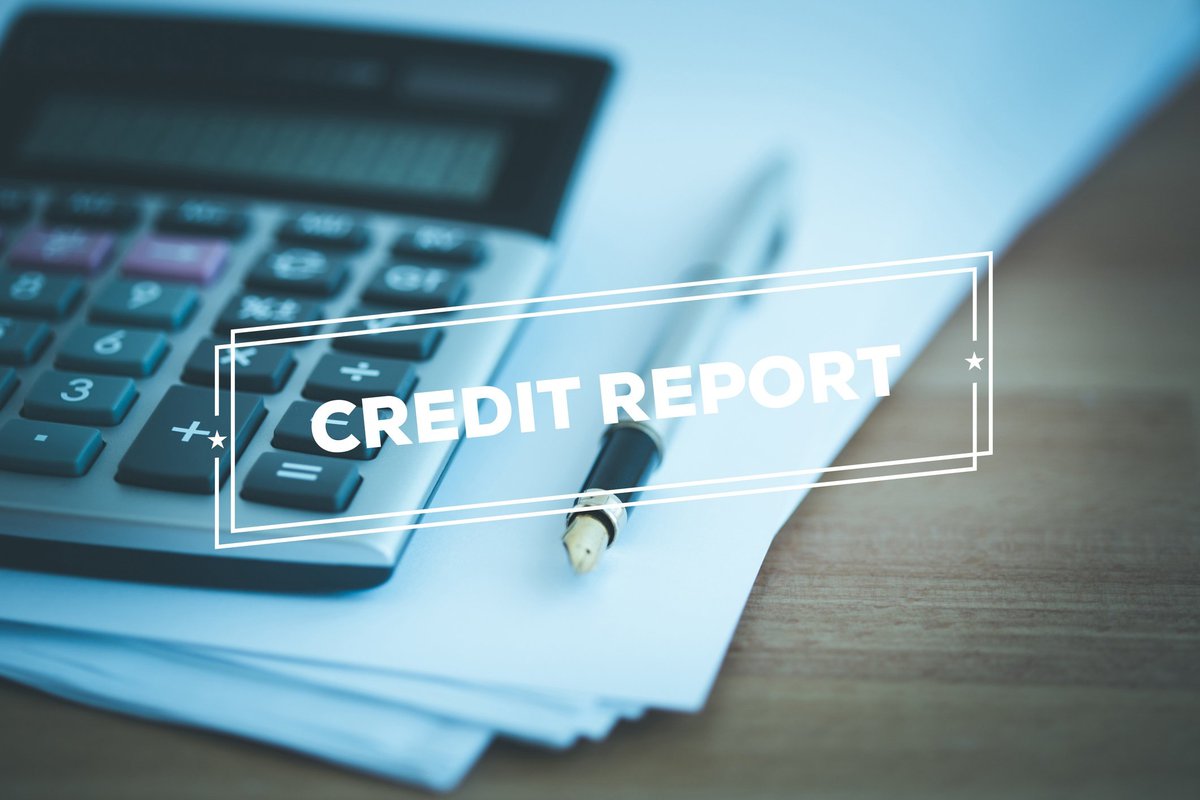 A calculator and pen on a stack of papers with the words credit report in the front.