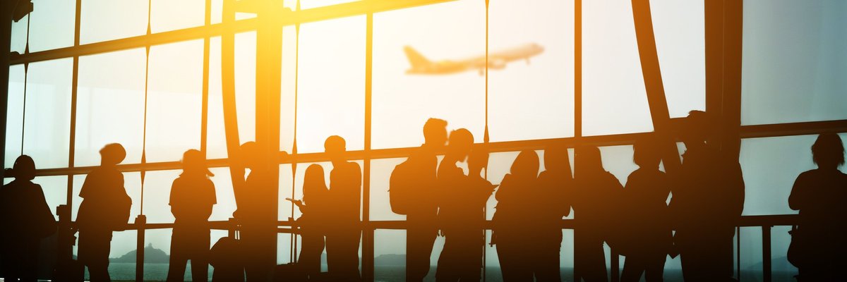 A crowd of people in front of a sunny airport window.