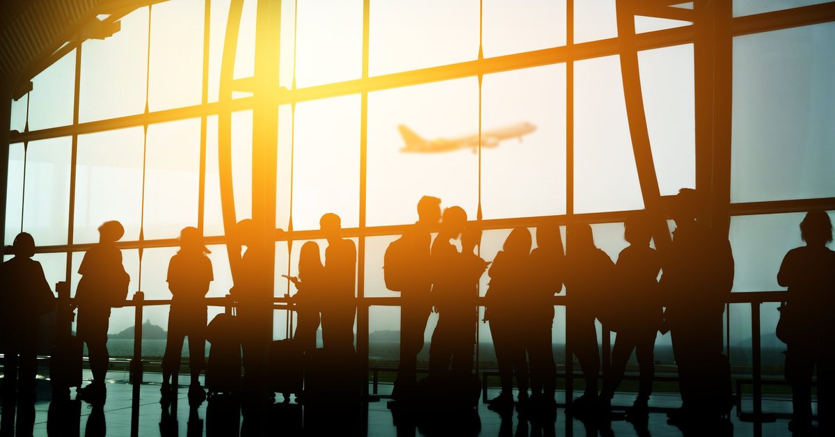 A crowd of people in front of a sunny airport window.