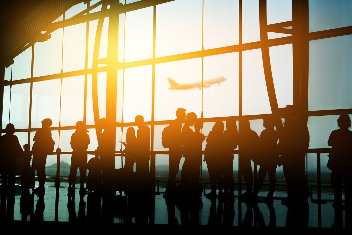 A crowd of people in front of a sunny airport window.
