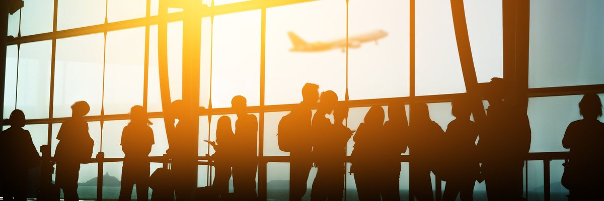 A crowd of people in front of a sunny airport window.