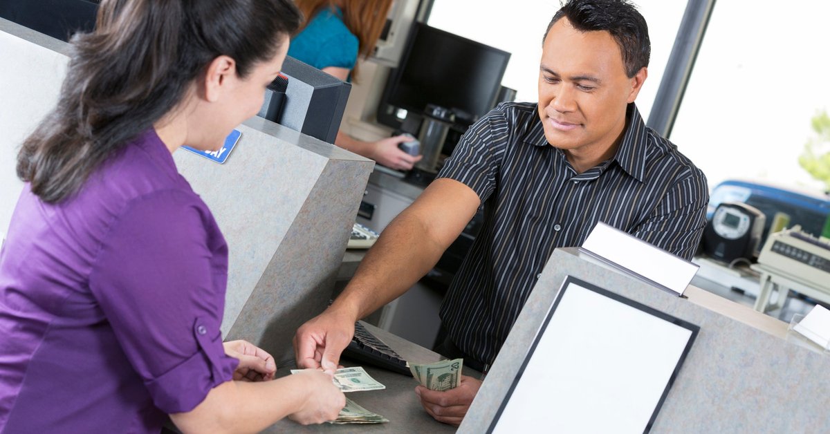 A young woman is at the bank. A teller is counting out her money.