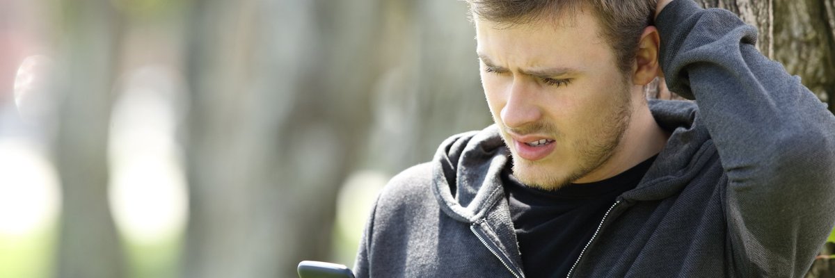 Man scratching his head and looking at a phone.