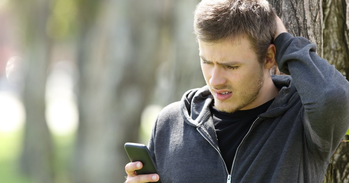 Man scratching his head and looking at a phone.