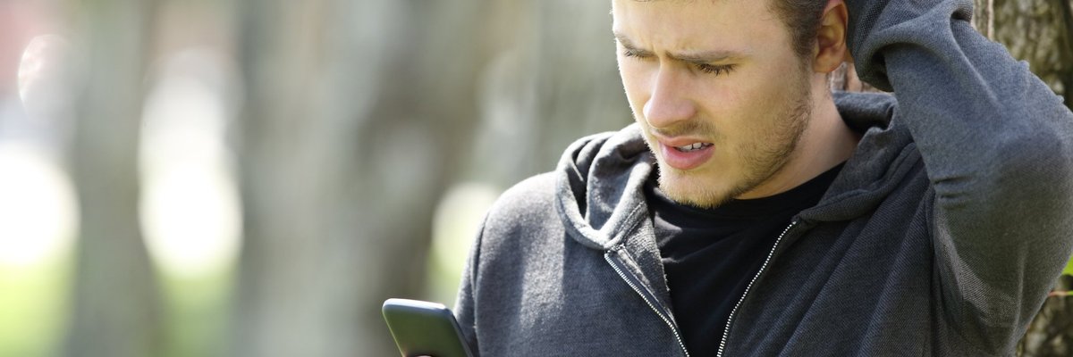Man scratching his head and looking at a phone.
