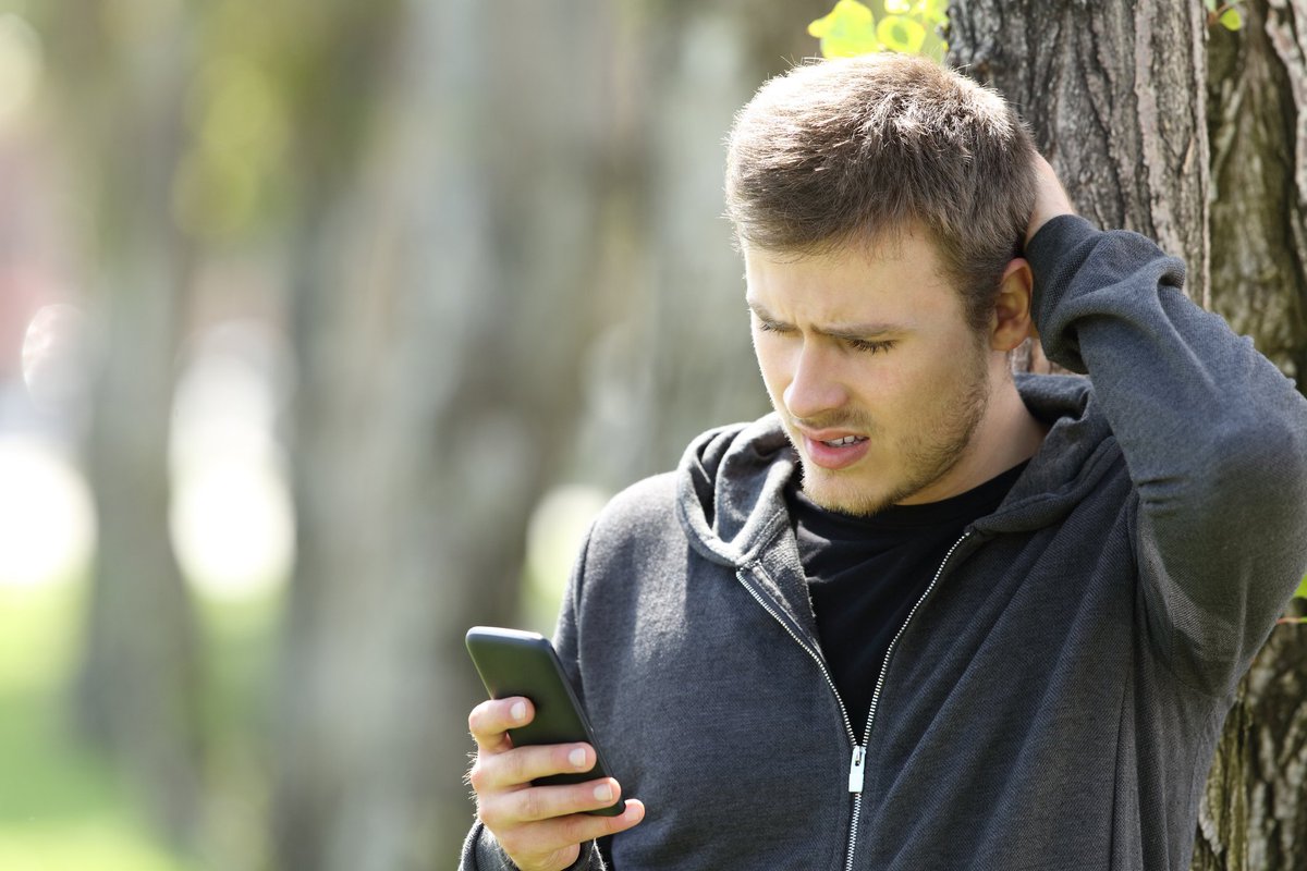 Man scratching his head and looking at a phone.