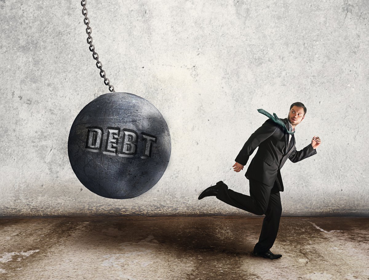 Man in suit running away from a wrecking ball that says DEBT