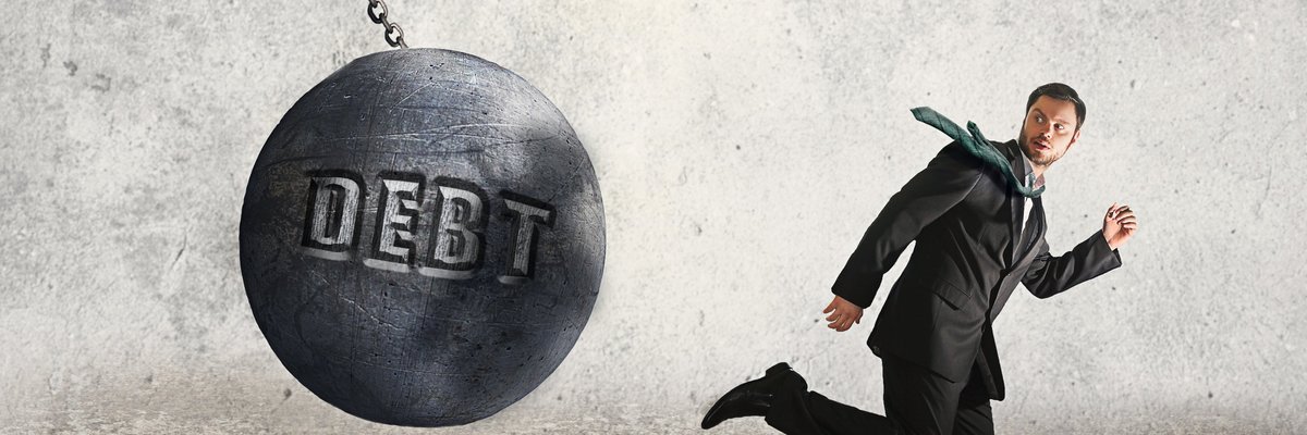 Man in suit running from a wrecking ball labeled Debt.
