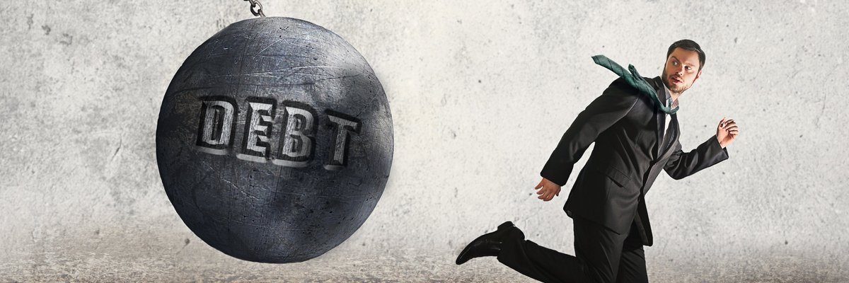 Man in suit running from a wrecking ball labeled Debt.