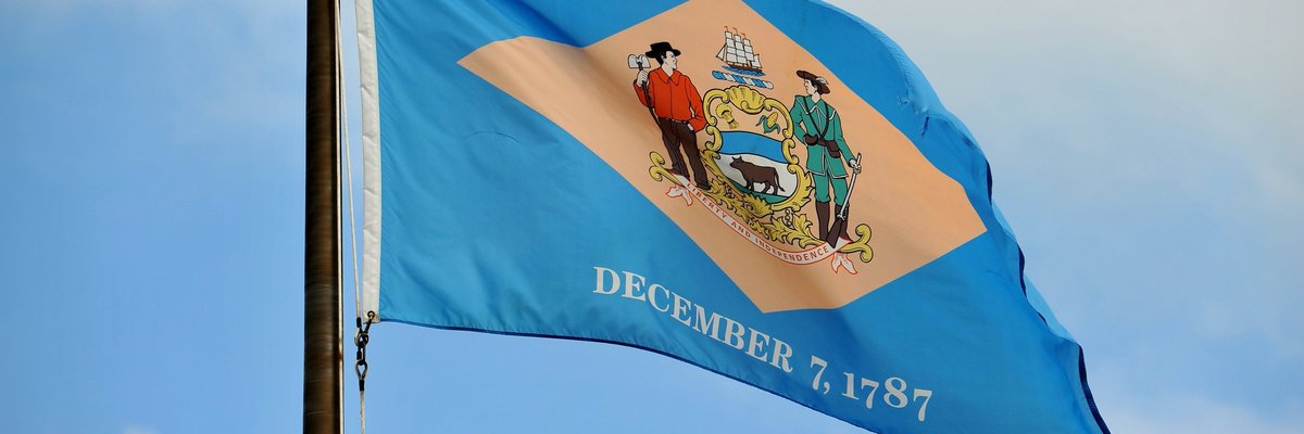 The Delaware state flag flying in front of a blue sky and white clouds.