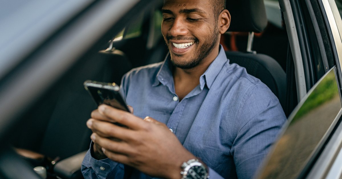 Driver sitting in driver's seat of vehicle and usince cellphone.