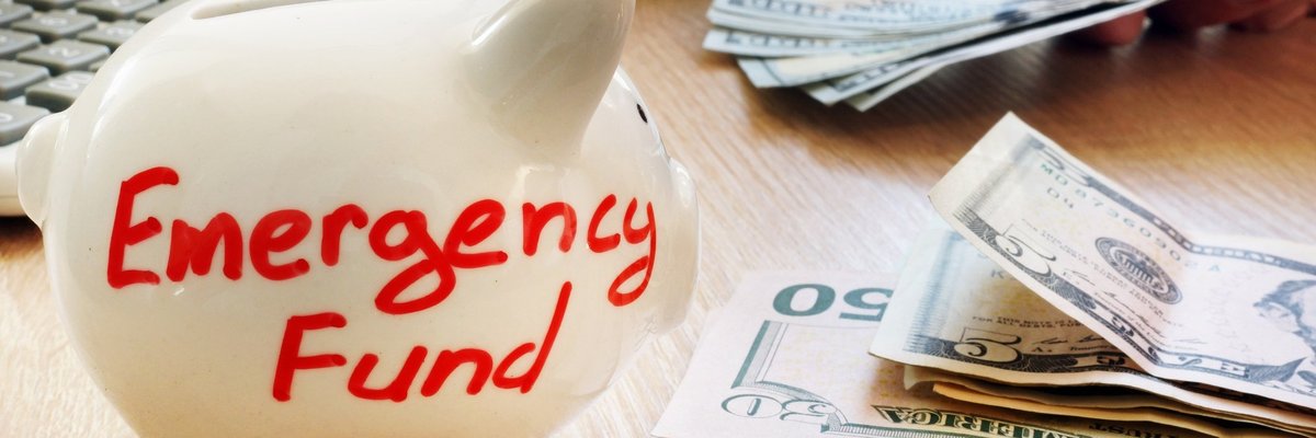 A white piggy bank that says emergency fund next to a stack of U.S. currency.