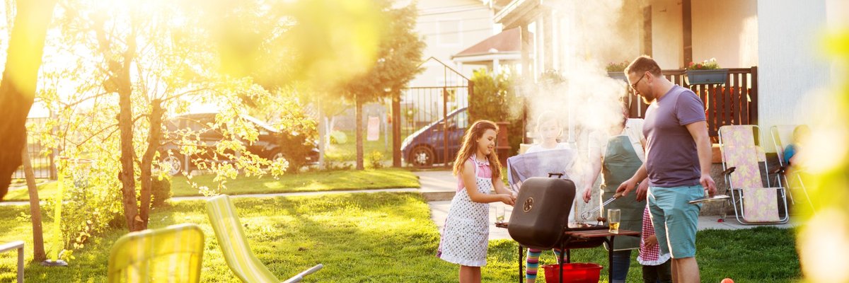 A family barbecuing in a sunny backyard.