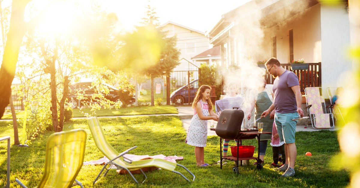 A family barbecuing in a sunny backyard.