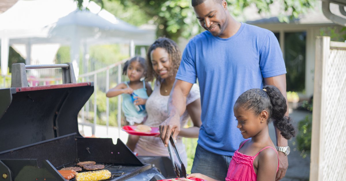 Family grilling hamburgers, hotdogs, and corn in back yard.