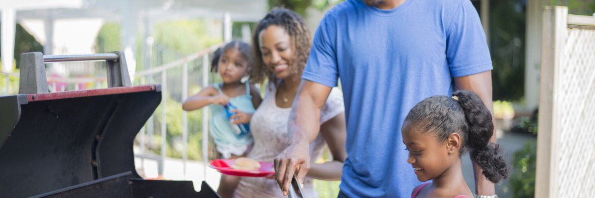 Family grilling hamburgers, hotdogs, and corn in back yard.