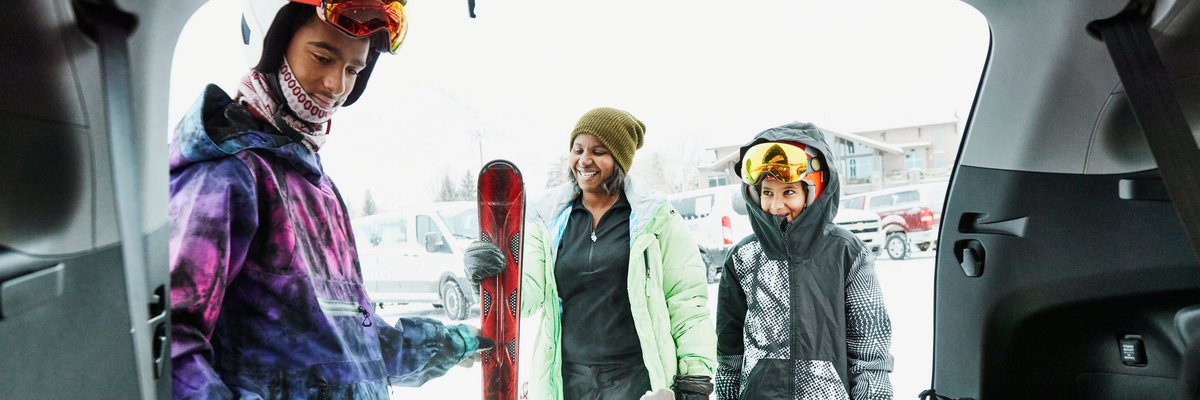 Family unpacking ski gear from car.