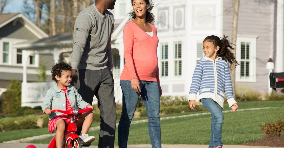 Couple walking through suburban neighborhood with youngest child riding a tricycle.