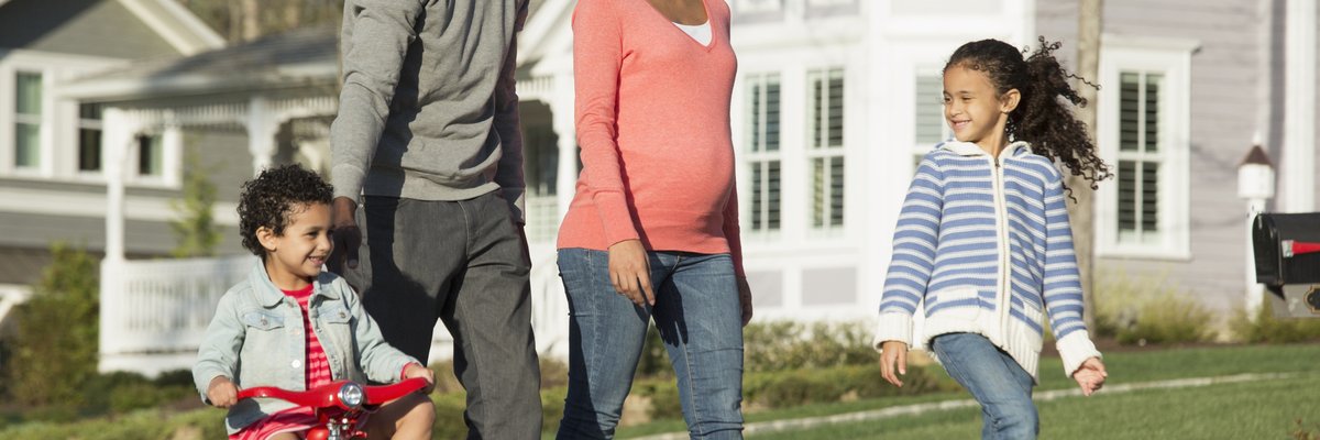 Couple walking through suburban neighborhood with youngest child riding a tricycle.