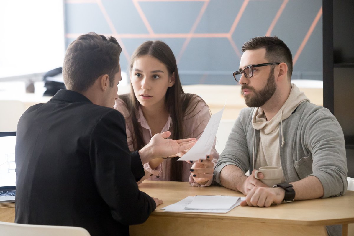 Frustrated couple pointing at paperwork with business man at desk.