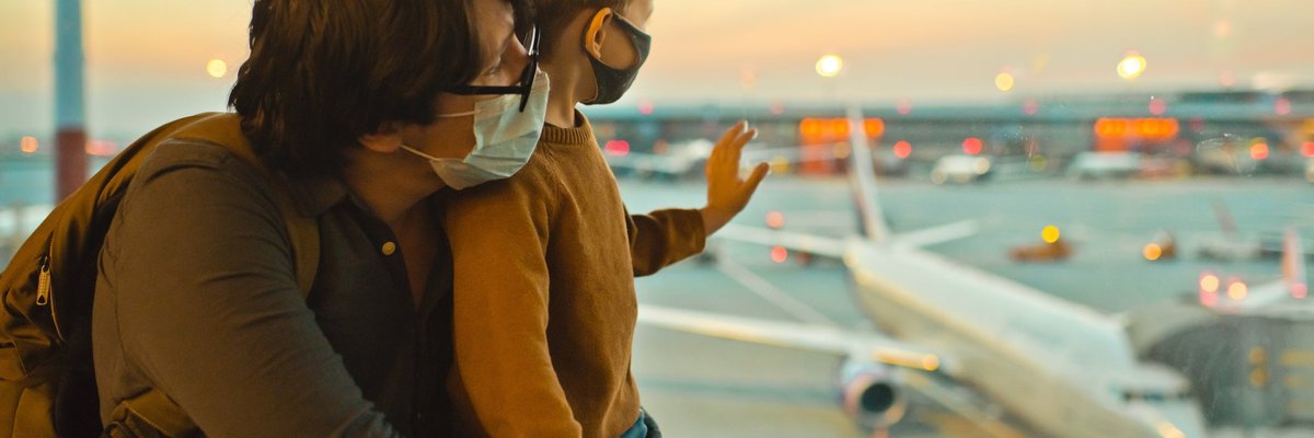 Father and son in masks looking out airport window.