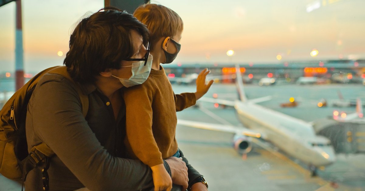 Father and son in masks looking out airport window.