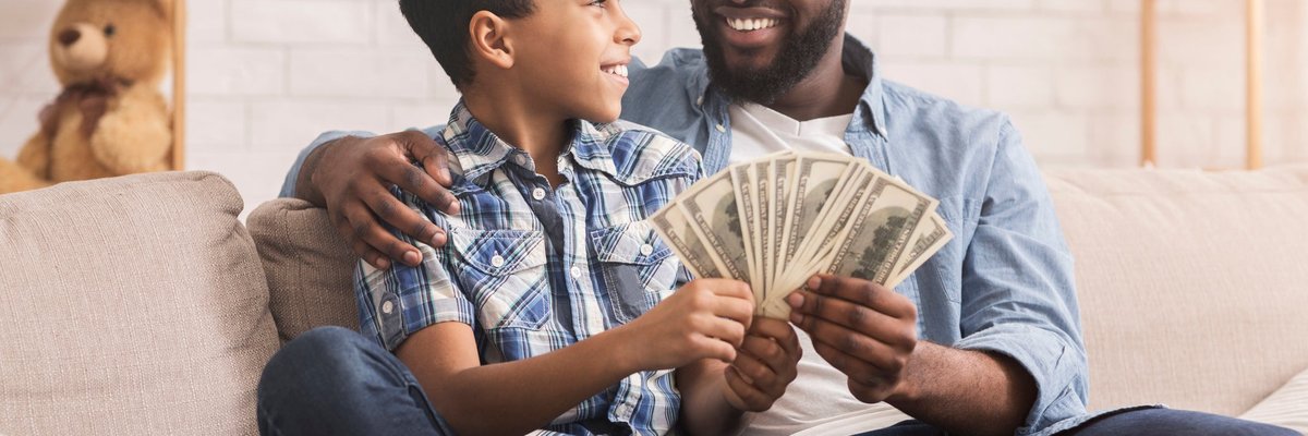 Father and son sit on the couch together holding cash.