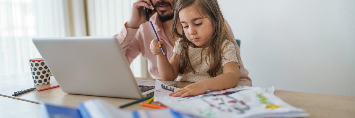 Father using laptop while on cell phone with young daughter coloring in his lap