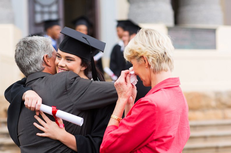 Female college grad hugging her dad next to her tearful mom.