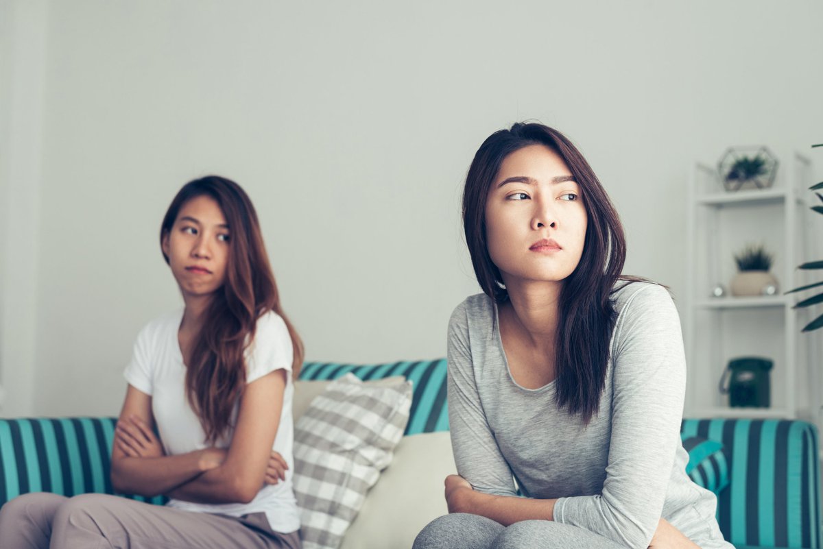 Two women having a disagreement on a couch with their arms crossed.