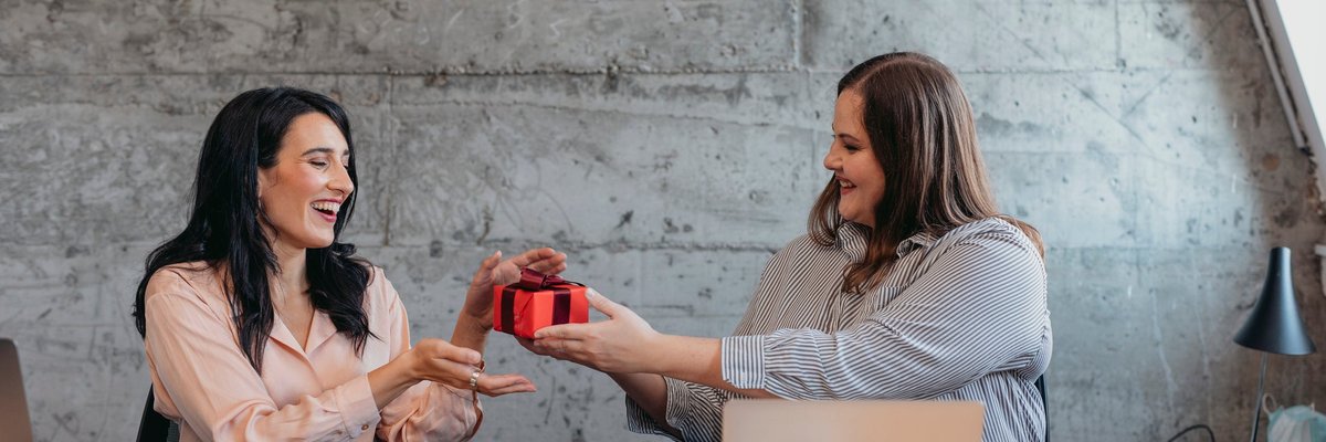 Female gives friend wrapped gift in an office setting.
