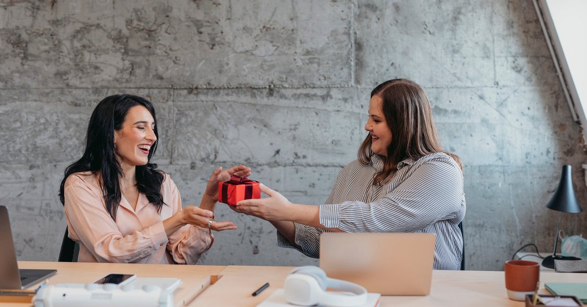 Female gives friend wrapped gift in an office setting.