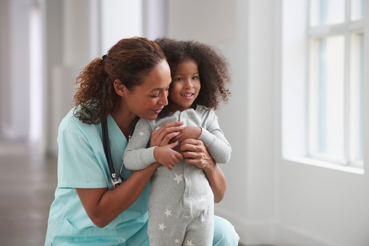 Female medical professional hugging young child.