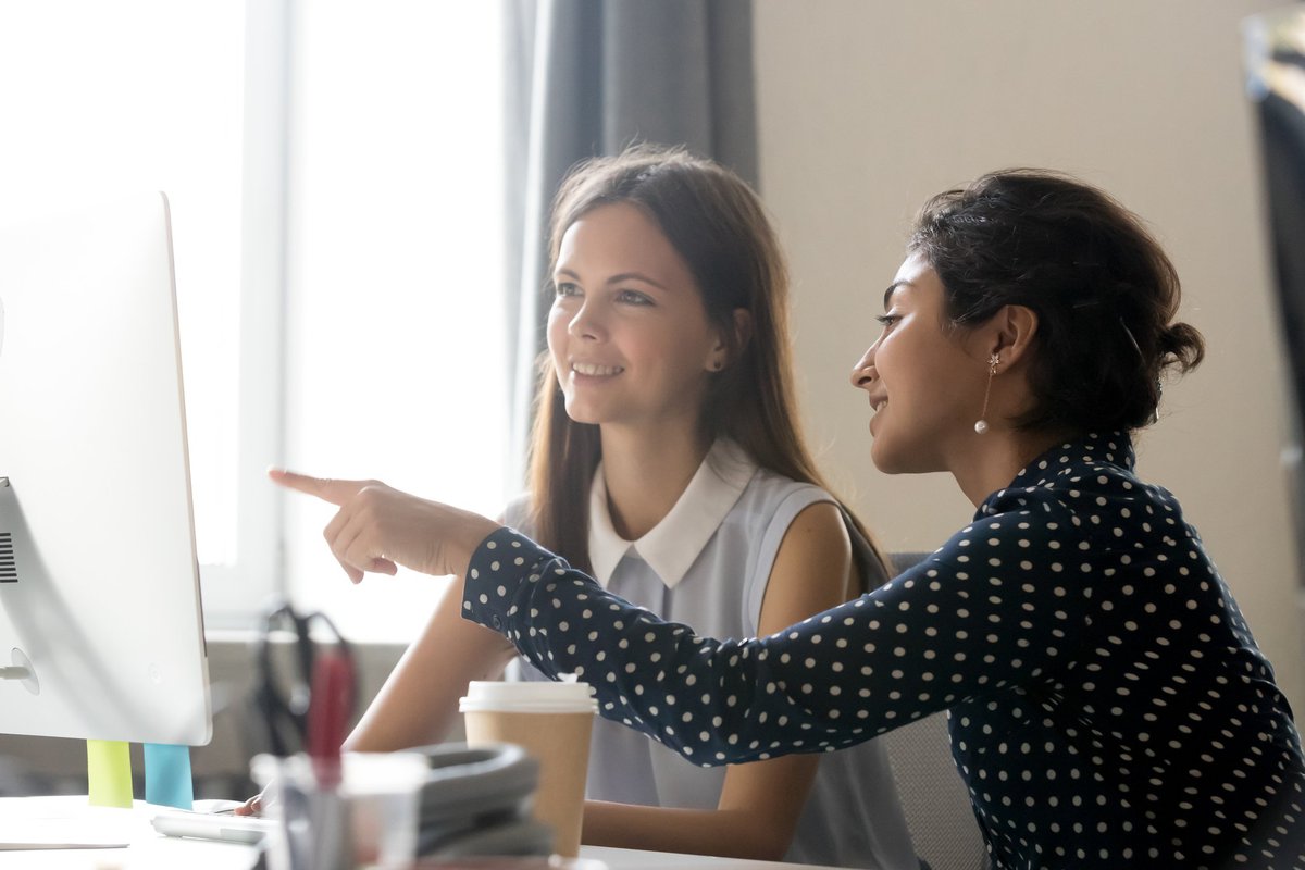 A woman mentoring a younger woman and pointing at computer.