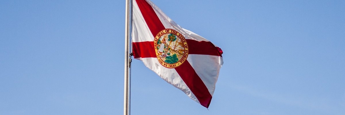 The Florida state flag flying in front of a blue sky.