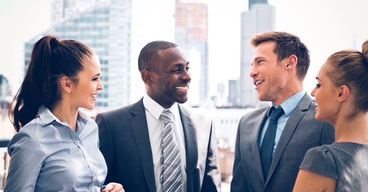 Four friends in business attire stand outside and laugh.